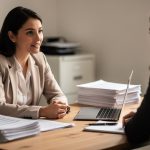 Une responsable des ressources humaines échange avec une personne d’une agence d’intérim dans un bureau de PME à Saint-Lô, autour de documents de recrutement et d’un ordinateur.