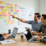 Une équipe marketing se réunit autour d’une table dans un bureau moderne, face à un mur couvert de post-it colorés et de graphiques de marque, avec des ordinateurs portables ouverts et une ambiance de travail collaborative.