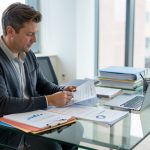 Un manager de PME examine des dossiers et planifie des recrutements lors d’une réunion RH dans un bureau moderne, avec ordinateur portable et documents sur un bureau en verre.
